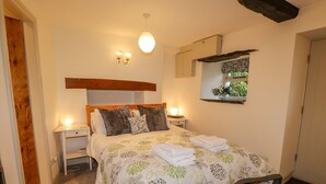 Un dormitorio con cabecera de madera, colcha estampada con flores, dos lámparas de noche y un espejo sobre la cama.