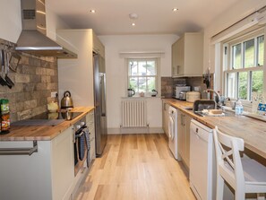 A modern kitchen with a stone backsplash, stainless steel appliances, wooden countertops, and a window providing natural light. - Highfold (Ambleside)