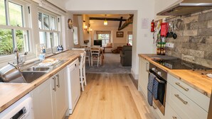 Una cocina moderna con armarios blancos, encimeras de madera y una isla central. Hay una zona de comedor con mesa y sillas, y vistas al exterior a través de amplios ventanales.