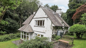 A white house with a steeply pitched roof, a visible chimney, and a small porch with a bench. - Miyanli (Windermere)