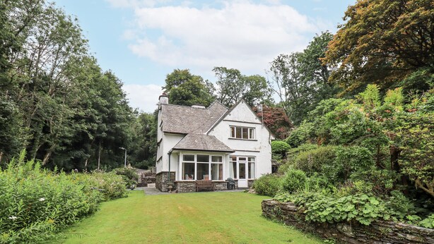 A white two-story house with a stone foundation, surrounded by lush greenery and a well-maintained lawn. - Miyanli (Windermere)