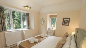 A bedroom with a large bed, a bedside table with a lamp, a window with curtains, and a radiator. - Miyanli (Windermere)