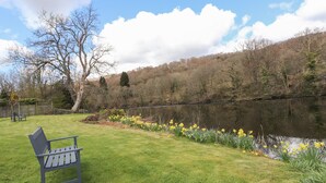 A bench in a grassy area beside a lake, surrounded by trees and yellow flowers.
