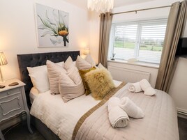 Una cama bien hecha con cabecera, almohadas y un suave plaid. Hay un cuadro en la pared sobre la cama y una ventana con cortinas.