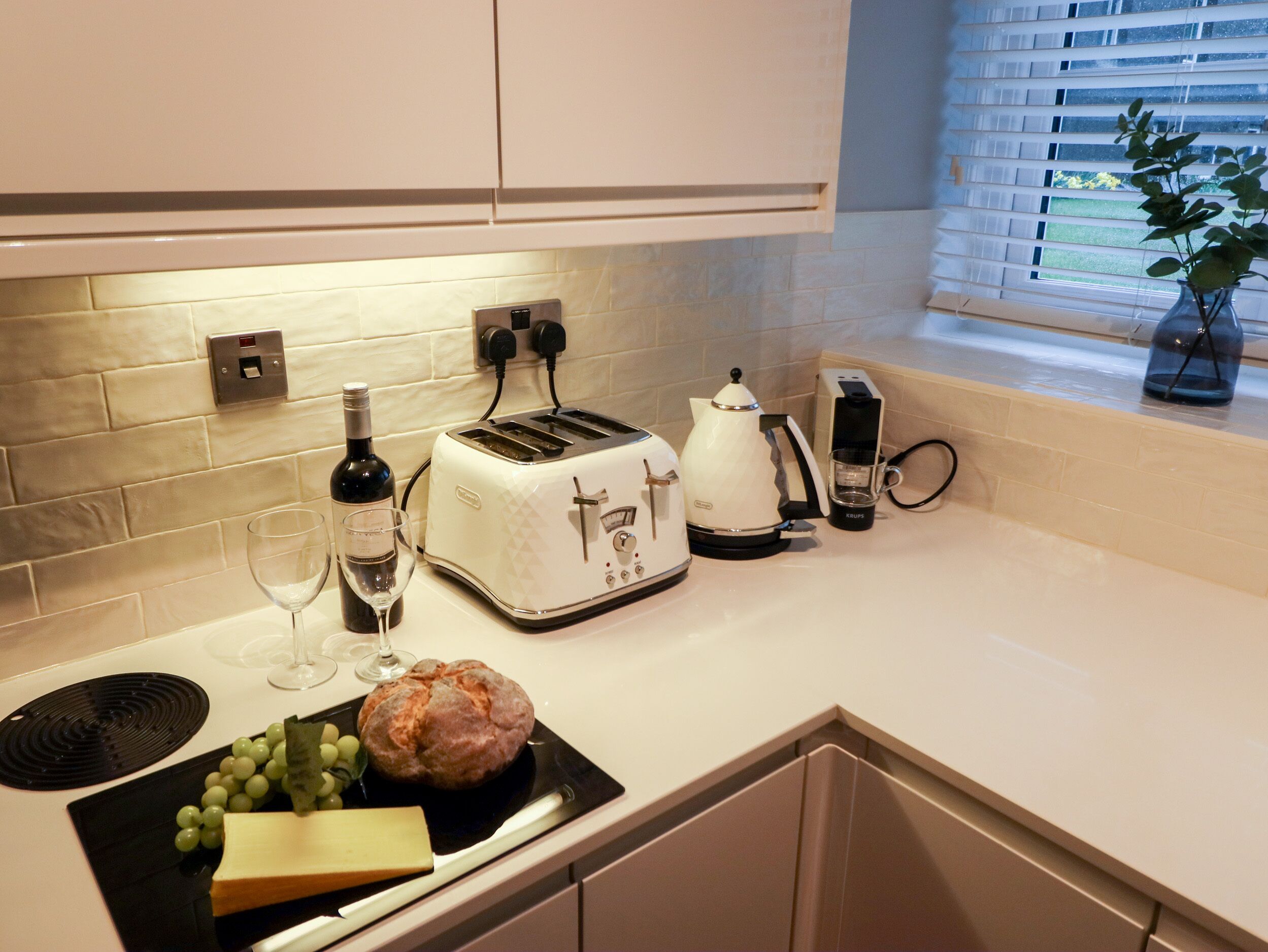 Uma cozinha com torradeira, cafeteira, uma garrafa de vinho e uma barra de pão no balcão.