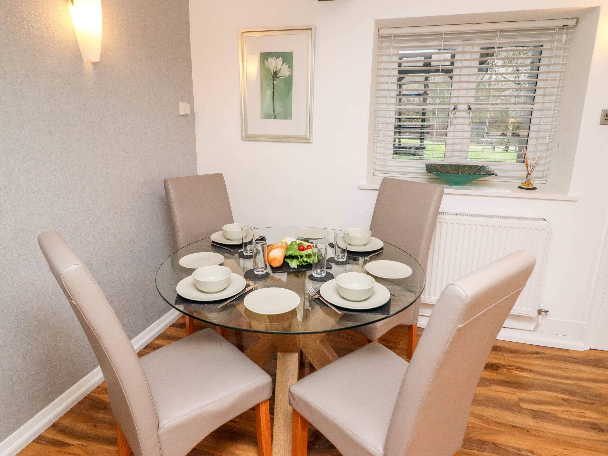 A dining area with a round glass table, four chairs, and a window with blinds.