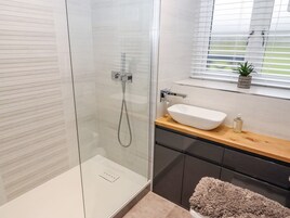Un baño moderno con cabina de ducha de vidrio, tocador de madera con lavabo y ventana con persianas.