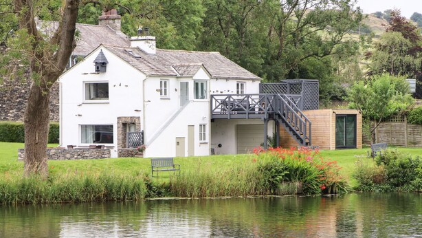 A white house with a stone facade, a wooden deck, and a staircase leading to a wooden cabin.