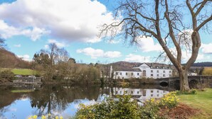 A white building with a 'Swan Hotel' sign, a bridge, and a calm lake reflecting the sky.