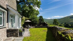 A stone house with a stone wall and a grassy yard. - Thyme Out (Windermere)