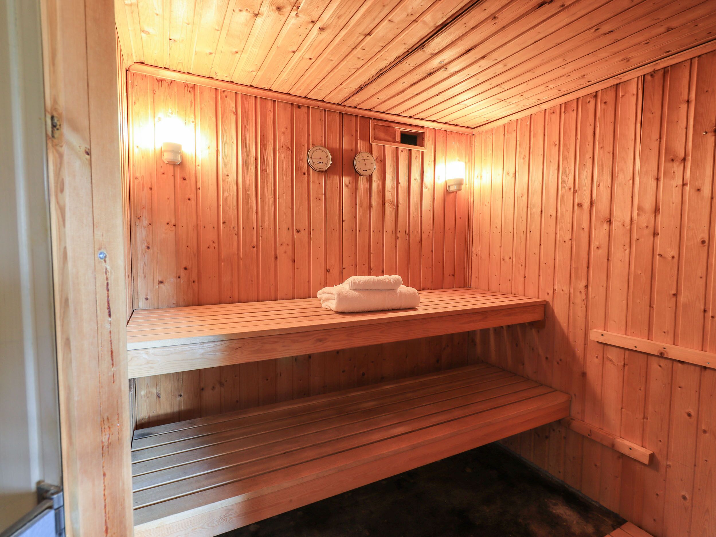 A wooden sauna with benches, a towel rack, and wall-mounted clocks.