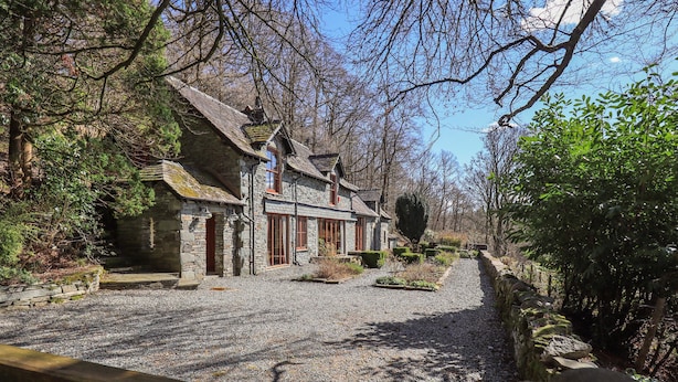 Ein Steinhaus mit Schotterauffahrt, umgeben von Bäumen und einem Holzzaun.