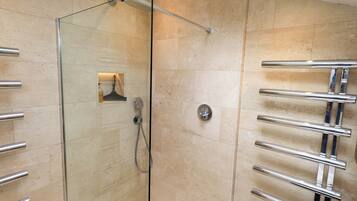 Un baño moderno con ducha de vidrio, toallero empotrado y secador de manos en la pared.