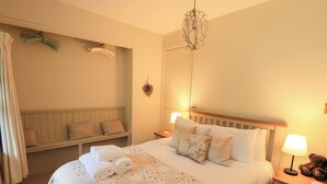 Ein ordentlich bezogenes Bett mit floralem Bettzeug, eine Nachttischlampe und ein Nachttisch mit Teddybär.