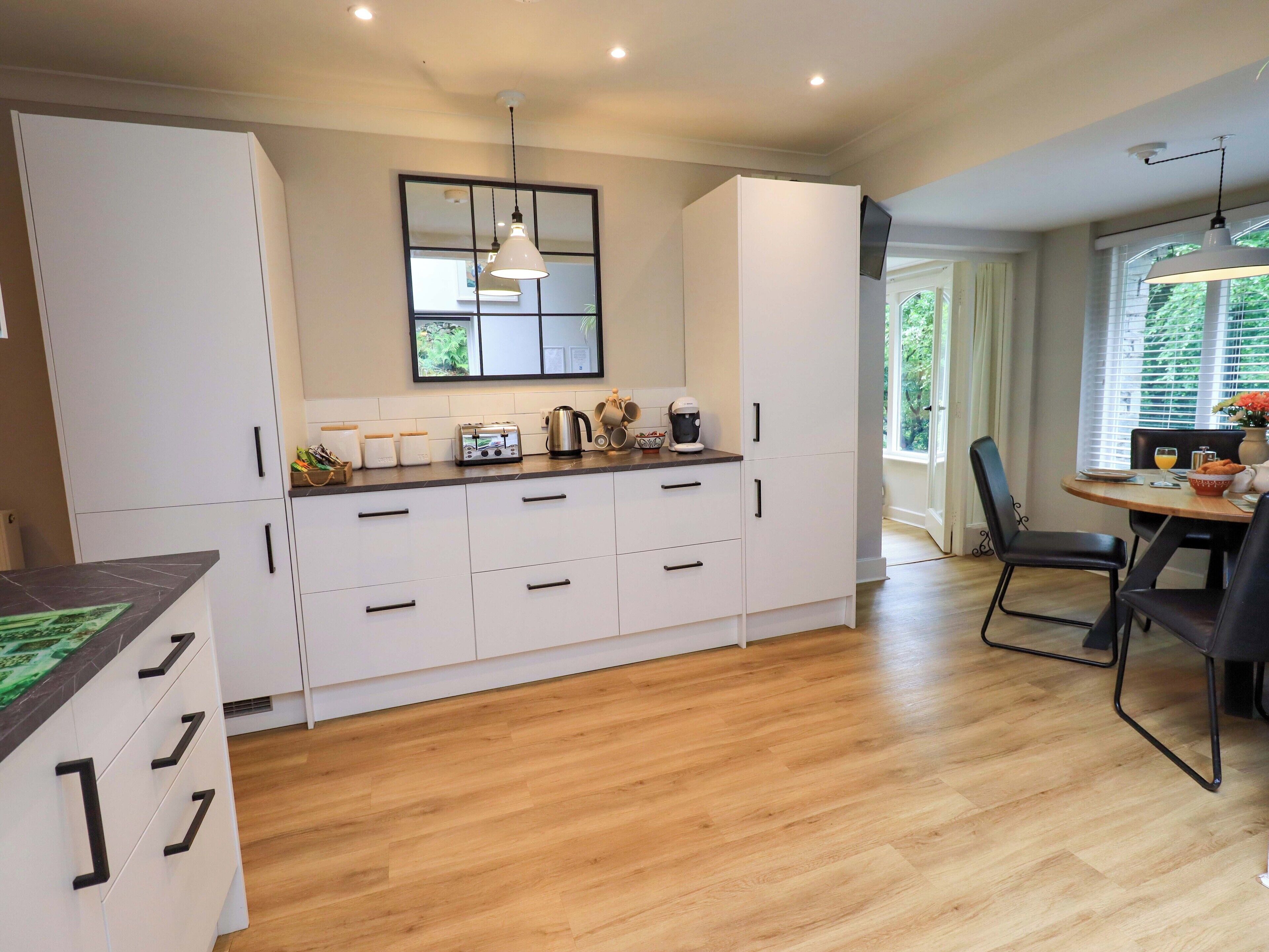 Une cuisine moderne avec des meubles blancs, un plan de travail en bois et un coin repas comprenant une table et des chaises.