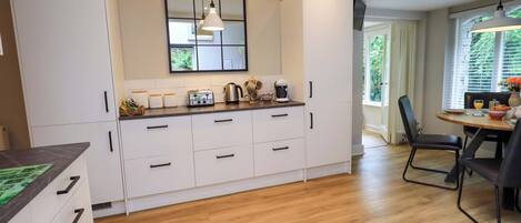 Une cuisine moderne avec des meubles blancs, un plan de travail en bois et un coin repas comprenant une table et des chaises.