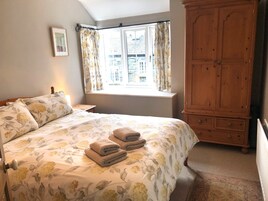 Un dormitorio con cama, ventana con cortinas, armario de madera y radiador.