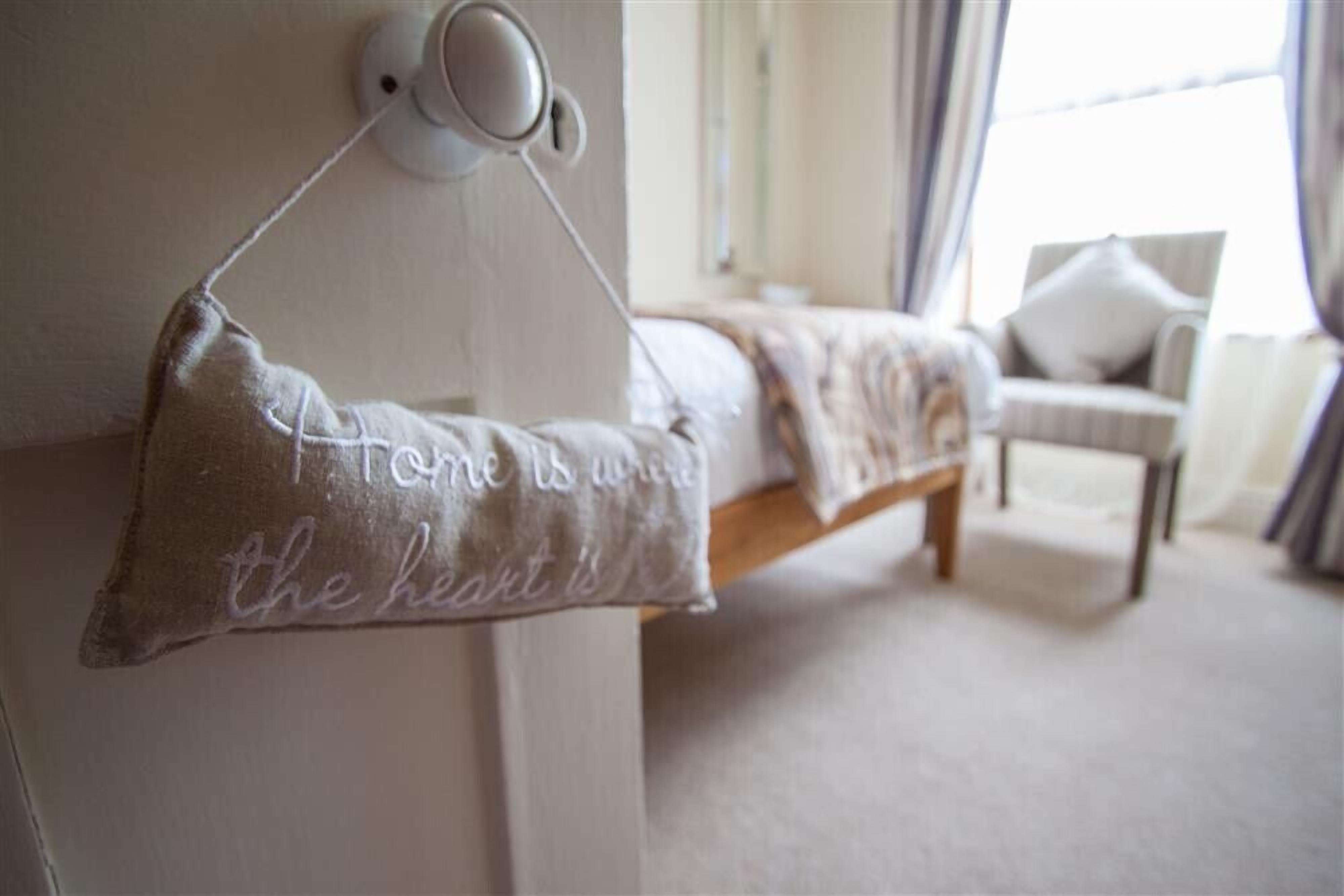 A bedroom with a bed, a bedside lamp, and a pillow with a quote.