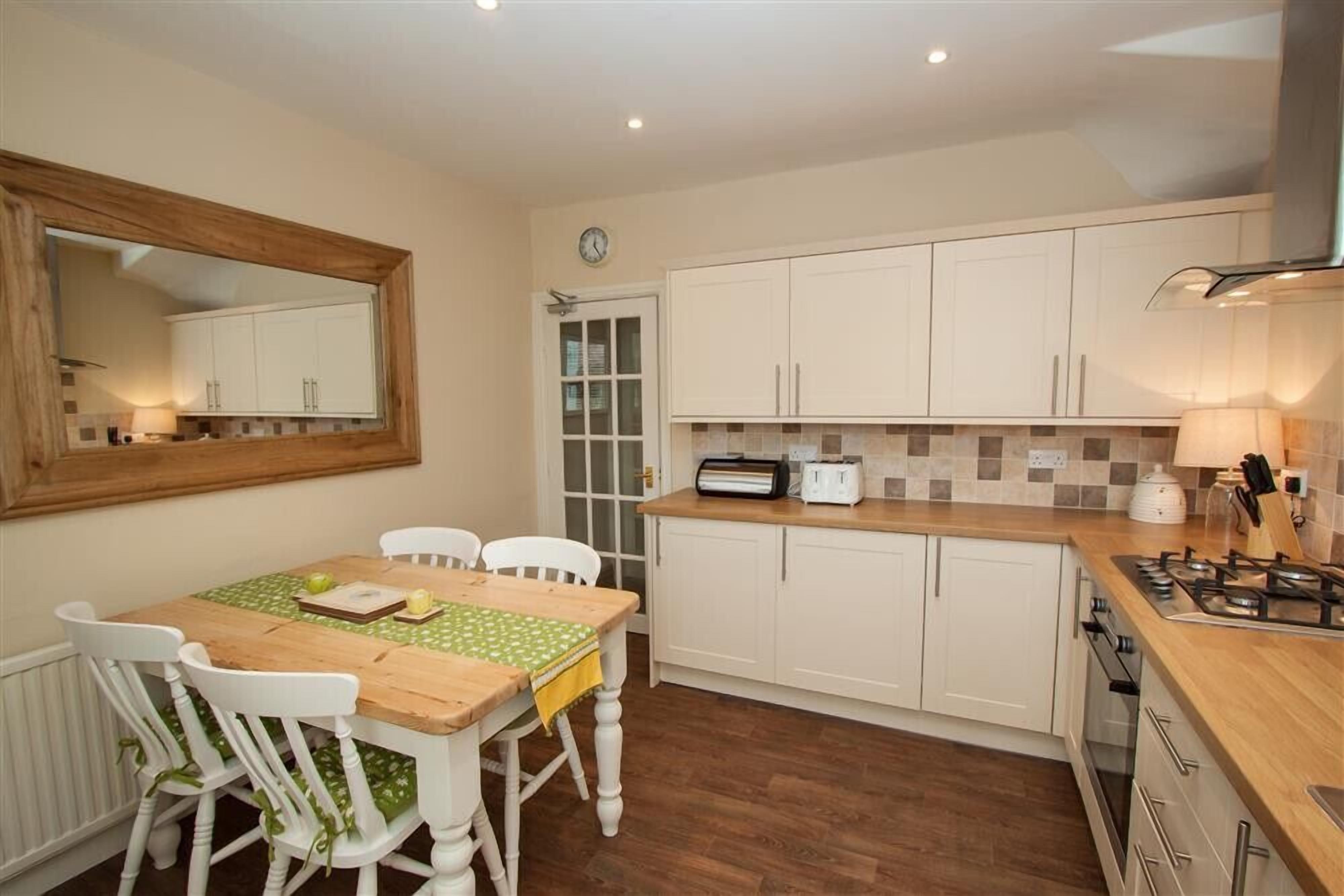A compact kitchen with white cabinets, a wooden table, and a green tablecloth.