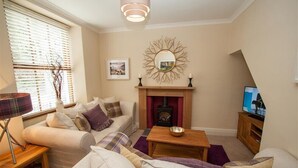 A cozy living room with a fireplace, a sofa set, a coffee table, and a television. - Acorn Cottage (Ambleside)