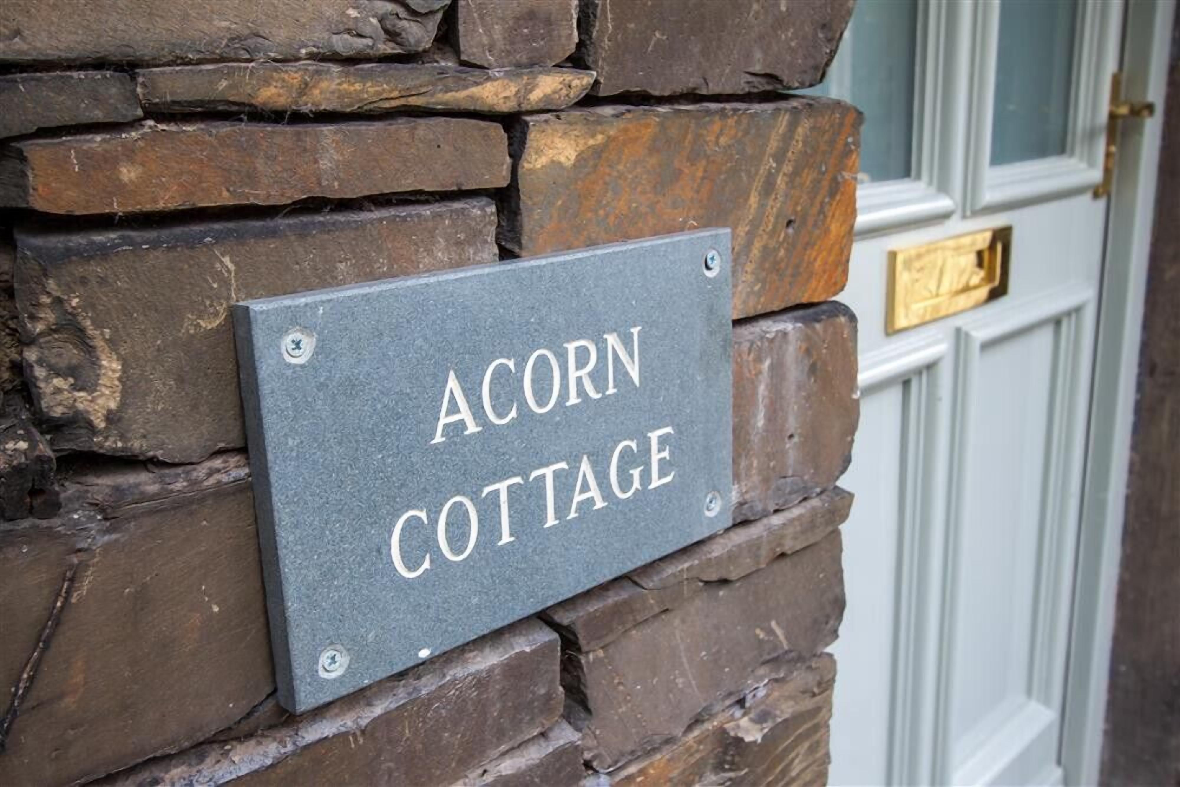 A sign reading "ACORN COTTAGE" mounted on a stone wall.