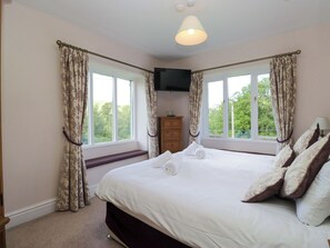 Ein Schlafzimmer mit Bett, Kommode, Fernseher und fensterbepflanzten Fenstern.