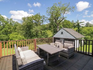 Eine Terrasse mit Korbmöbeln und einem kleinen Schuppen in einer grünen Landschaft.