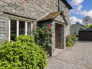 A stone building with a gravel driveway, a small porch, and pink flowers. - Elterwater Lodge (Ambleside)