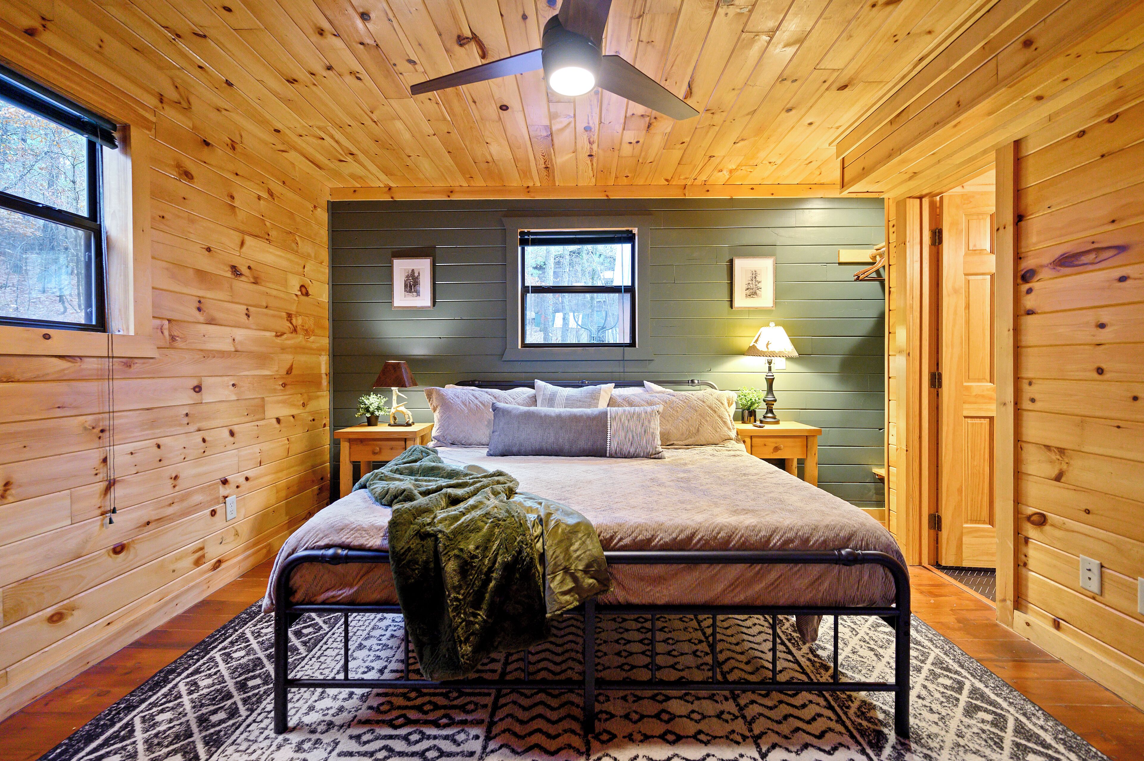 Ein Schlafzimmer einer Holzhütte mit Bett, Deckenventilator, Fenster und Tür.