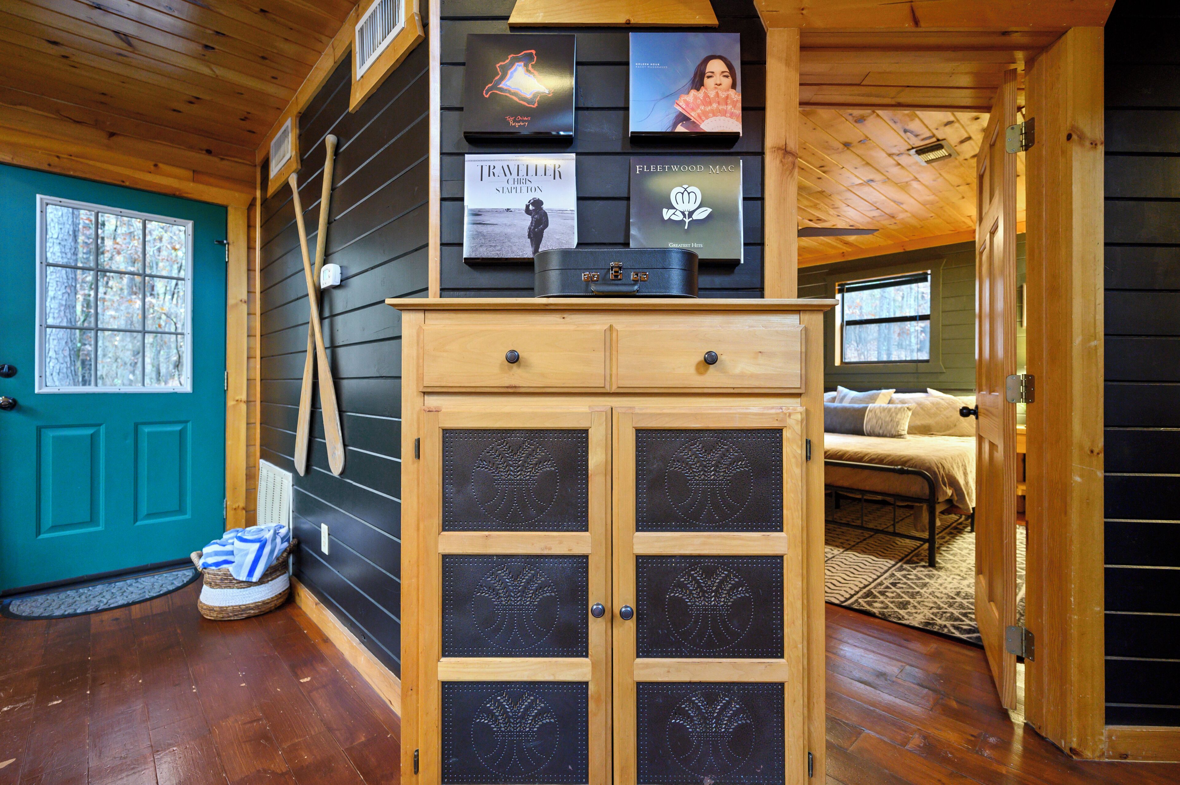 A cabin interior with a wooden cabinet, a teal door, and a bed with a patterned rug.