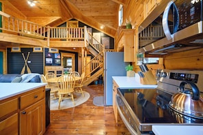 A wooden cabin interior with a kitchen, dining area, and a loft bedroom.