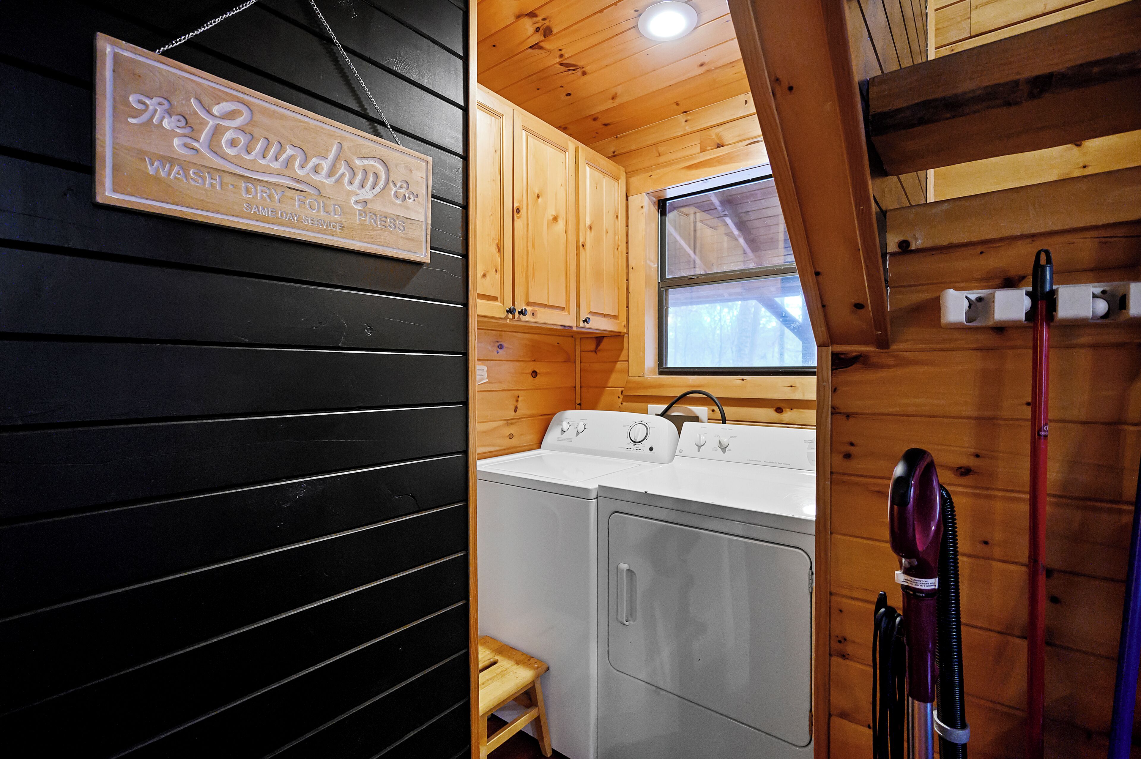 A laundry room with wooden cabinets, a washing machine, a dryer, and a small stool.