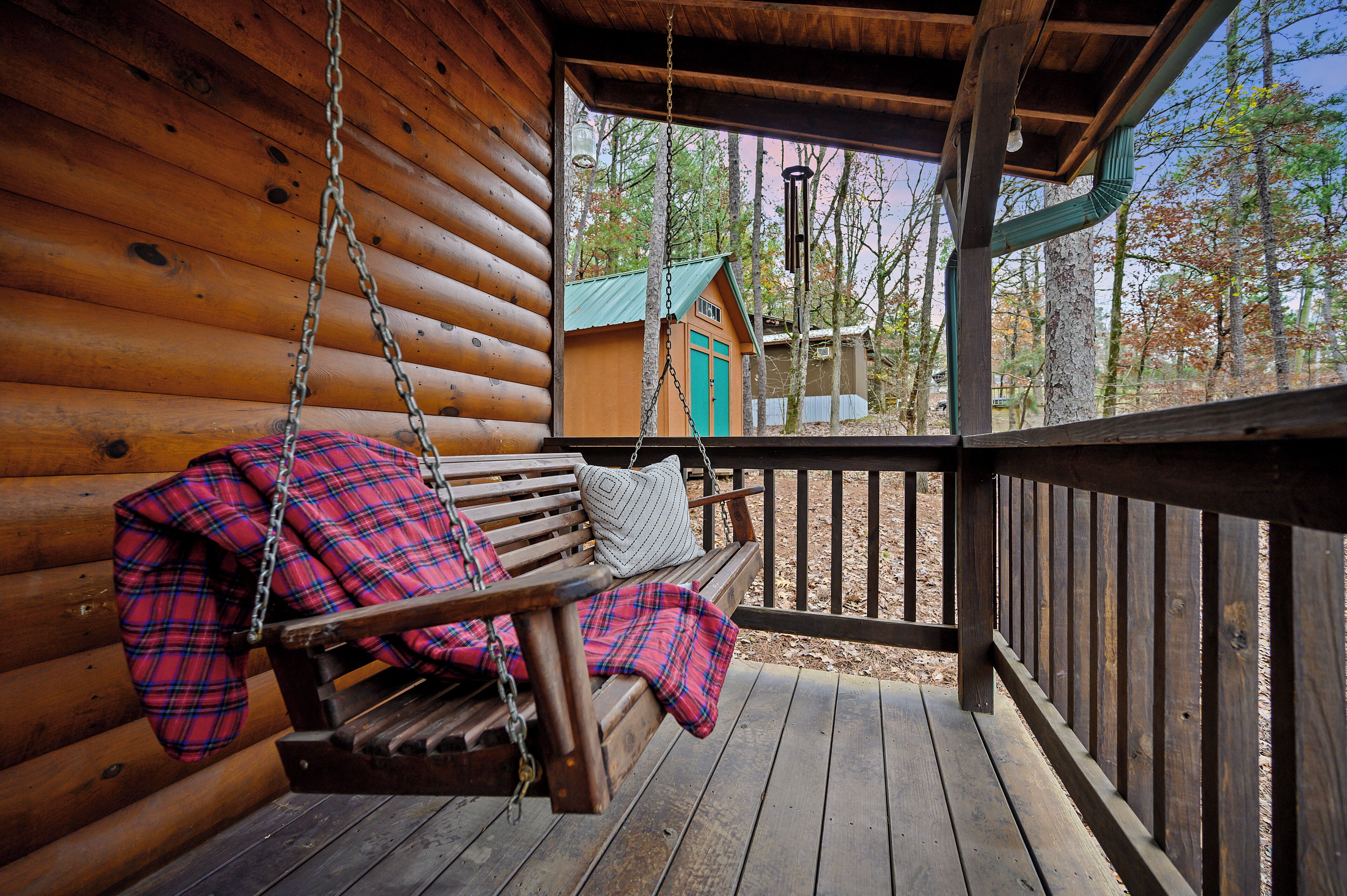A wooden cabin with a porch, a swing, and a view of a cabin in the background.