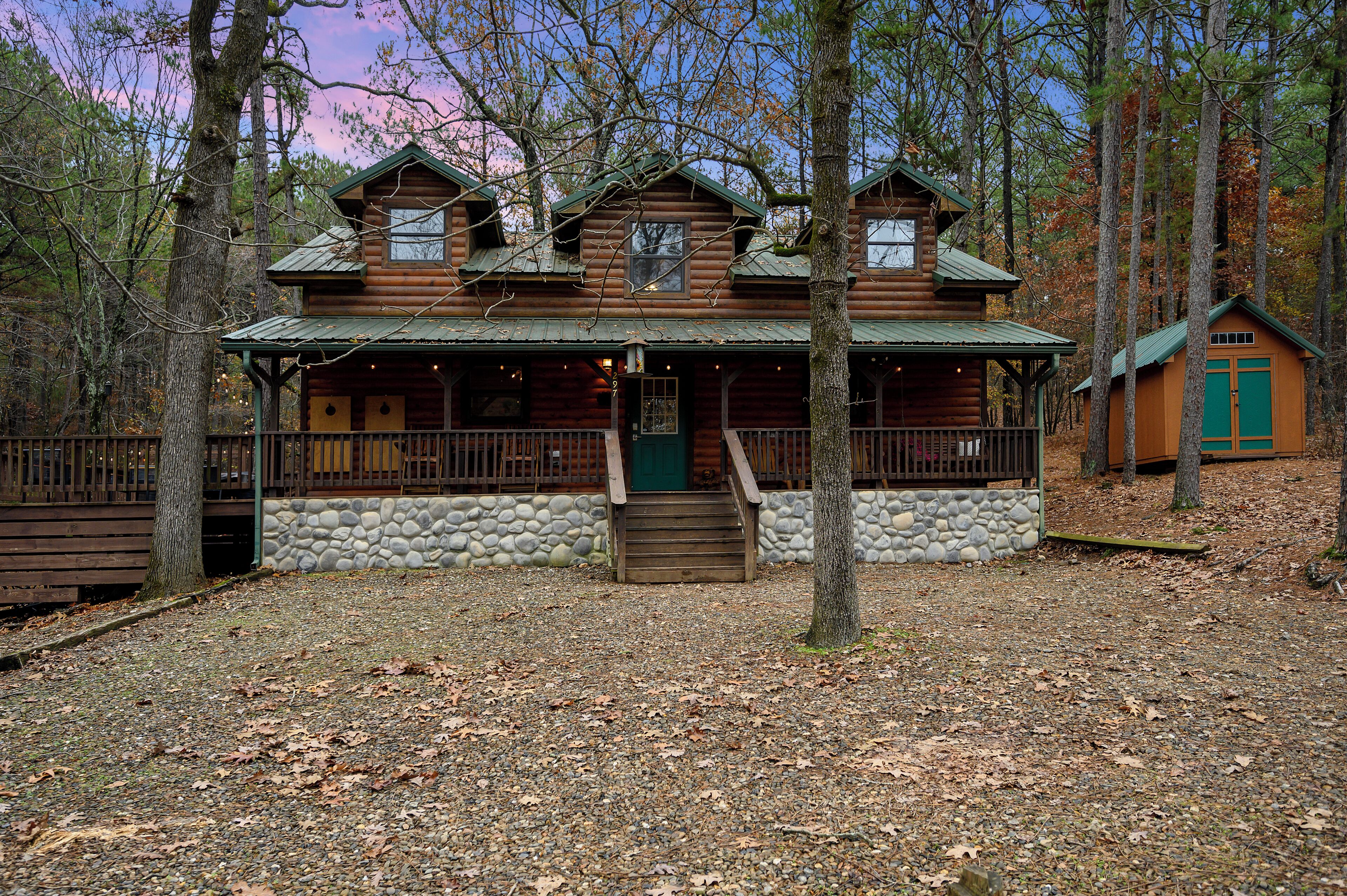 Ein rustikales Holzhaus mit Steinuntergrund, einer Veranda und einem separaten Gebäude mit grüner Flachdach.