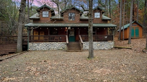 A rustic log cabin with a stone foundation, a porch, and a separate green-roofed building. - Cozy cabin located in Beavers Bend, close to Broken Bow lake, Casino (Broken Bow)