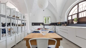 A spacious kitchen with a wooden dining table, white cabinets, and a large window. - 2320 Villa Ilse by Perle di Puglia (Andrano)