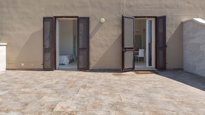 A building with two open doors leading to interior spaces, a tiled patio, and a wall with a textured finish. - 2292 Villetta Cielo Blu by Barbarhouse (Lecce)