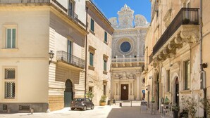 A street view with a historic building featuring ornate architecture, a car parked on the side, and a clear blue sky. - 2292 Villetta Cielo Blu by Barbarhouse (Lecce)