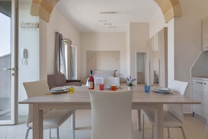 Un comedor moderno con una mesa de madera, sillas blancas y vistas a la cocina al fondo.