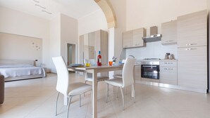 A modern, well-lit room with a dining table, chairs, a bed, and a kitchen area with cabinets and appliances. - 2292 Villetta Cielo Blu by Barbarhouse (Lecce)