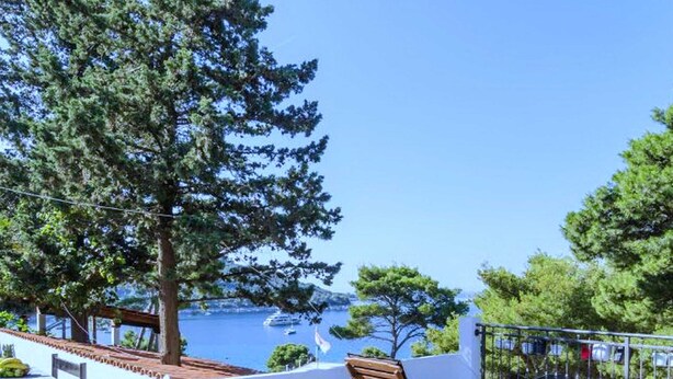 A terrace with a table and chairs, a wooden lounge chair, and a view of the sea. - Apartments Ammos (Mljet)