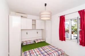 Une chambre à coucher avec un lit, un luminaire suspendu, une fenêtre avec des rideaux rouges et des armoires encastrées blanches.