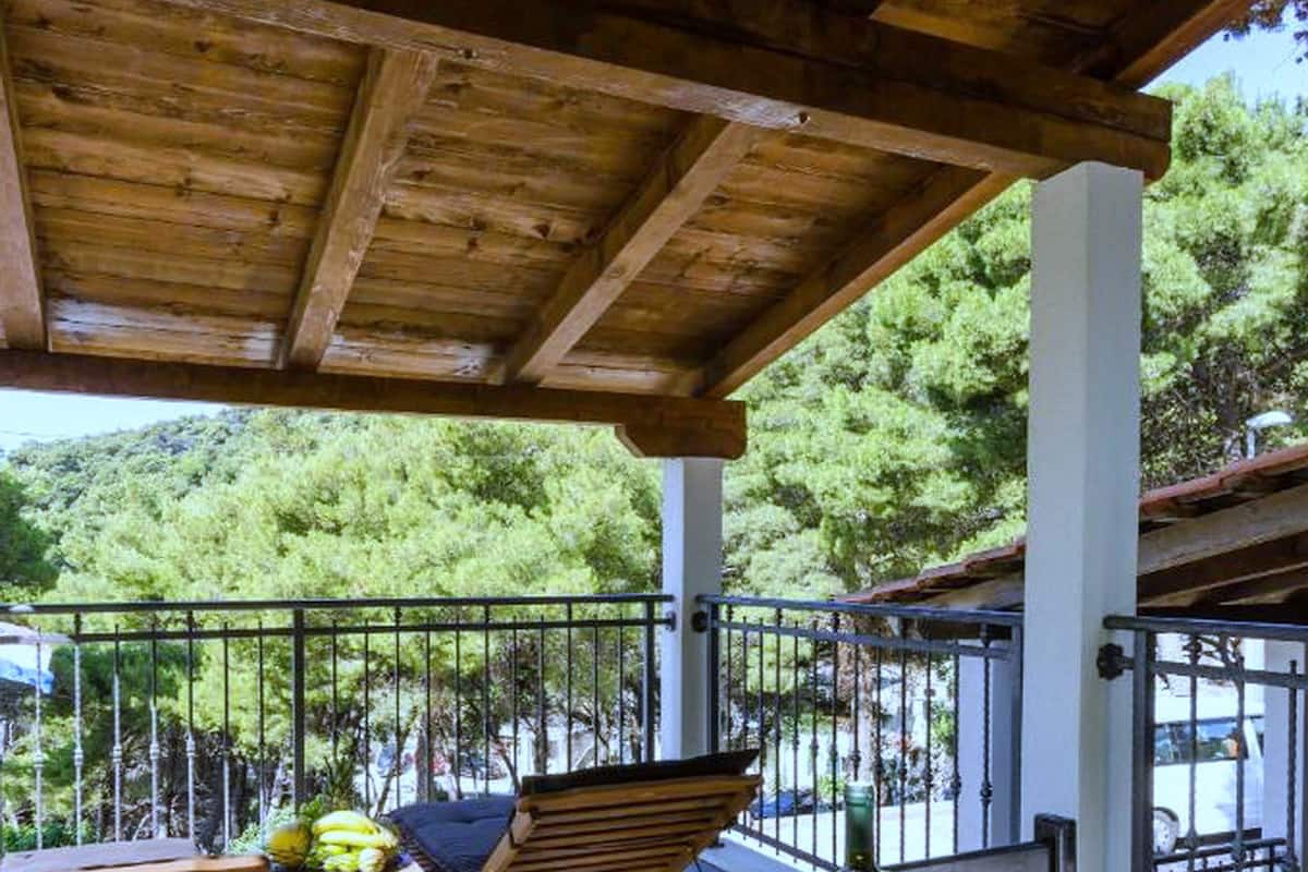 Une terrasse en bois avec des sièges d’extérieur, une table avec une bouteille, et une vue sur une colline boisée.