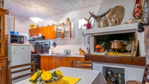 A kitchen with wooden cabinets, a microwave, and a dining table with a yellow placemat and a bowl of flowers. - Rooms Tupina By Paulina - Hostel (Zupa dubrovacka)