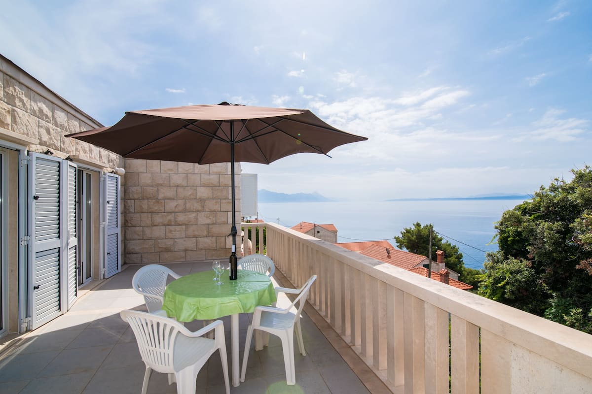 A balcony with a table and chairs, a table umbrella, and a view of the sea.