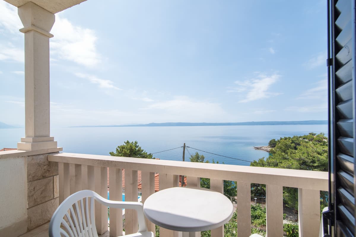 A balcony with a white chair and table, overlooking a body of water and greenery.