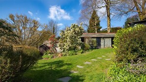 Een tuinpad dat leidt naar een stenen gebouw met een schuin dak, omgeven door weelderige begroeiing en bomen.