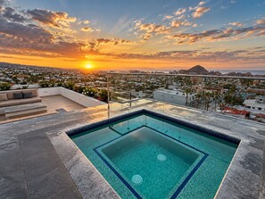 A rooftop pool with a clear view of a cityscape and a mountain at sunset.