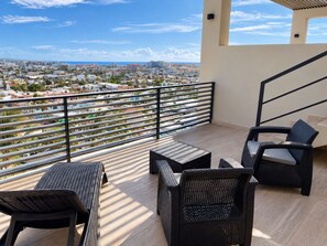 A balcony with wicker furniture, a view of a cityscape, and a railing.