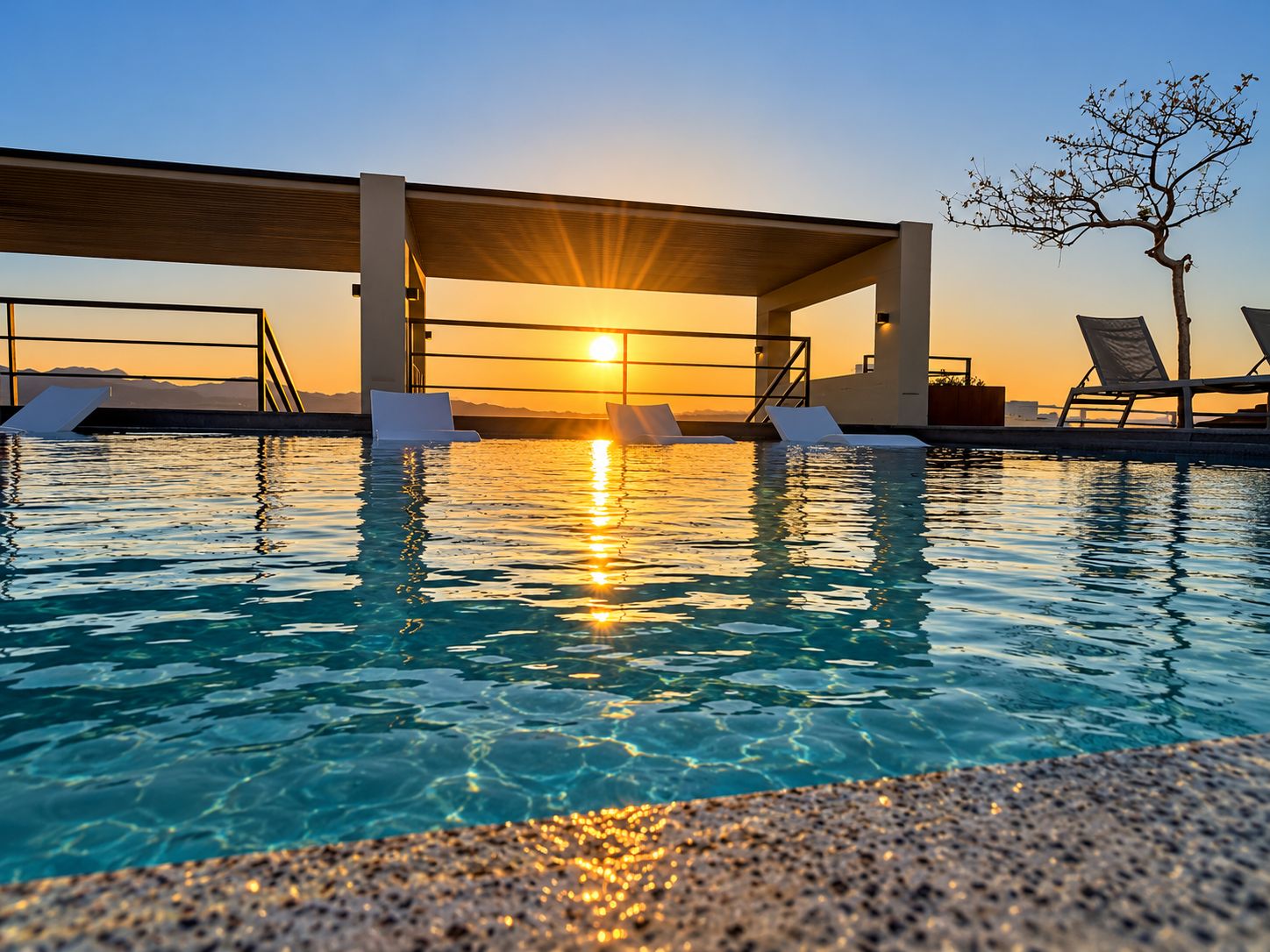 Piscina com espreguiçadeiras e vista para o pôr do sol.